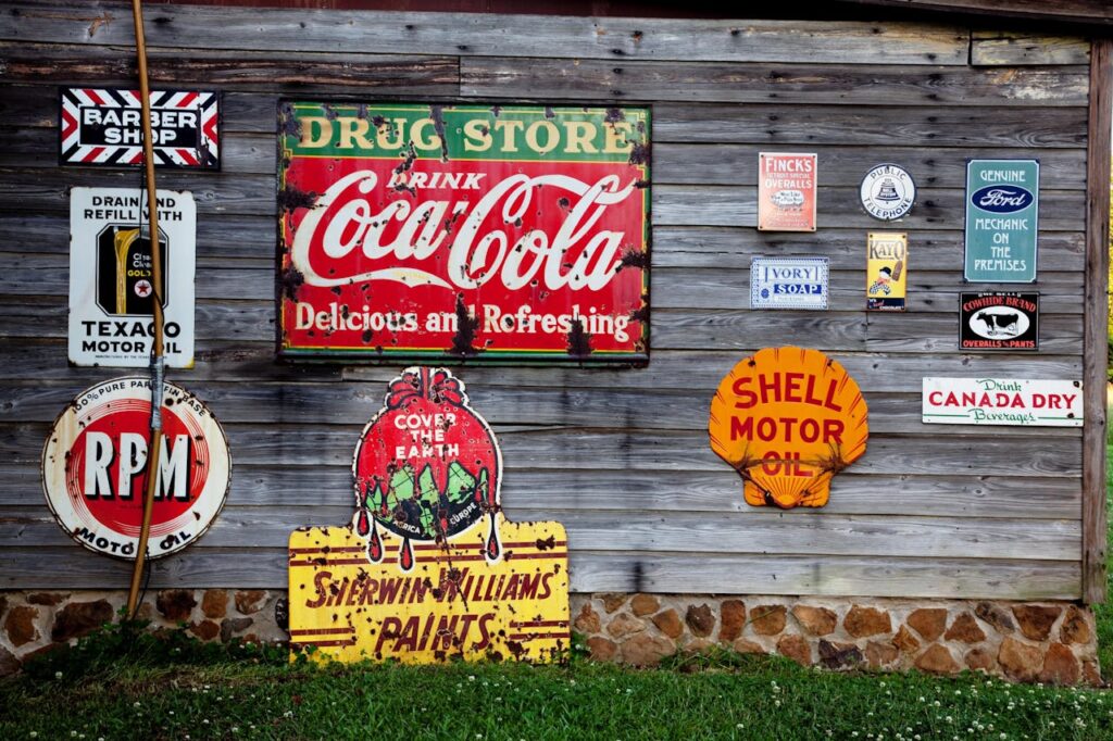 Collection of vintage advertising signs on rustic wooden wall showcasing classic brands.