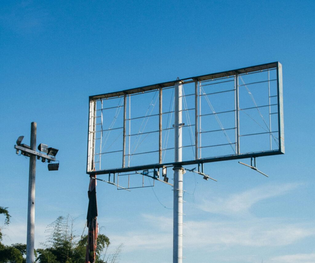 An empty metal billboard structure stands tall on a rural road under a clear blue sky.