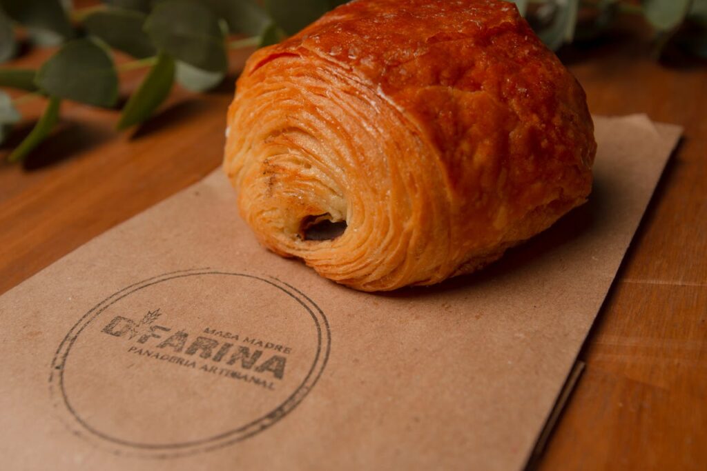 Delicious artisan pastry resting on a branded paper bag with green foliage in the background.