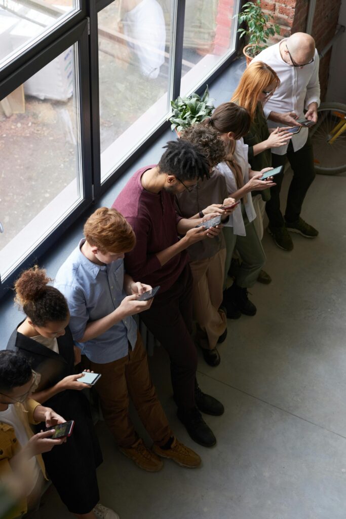 A group of diverse office workers standing by a window using smartphones, capturing modern workplace connectivity.